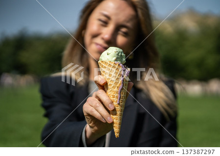 Cheerful positive woman posing with ice cream in hand, enjoying refreshing treat on summer day. Cheerful positive woman posing with ice cream in hand, enjoying refreshing treat on summer day. 137387297