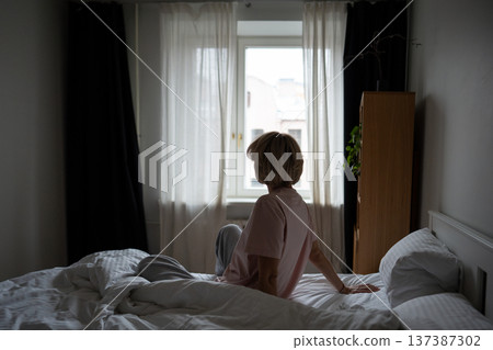 Calm woman sitting in bed in early morning after waking up, looking at window enjoying daylight. 137387302