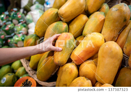 Customer inspects papaya firmness and color to test freshness at food market stall, healthy dieting Customer inspects papaya firmness and color to test freshness at food market stall, healthy dieting 137387323