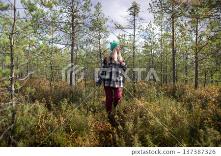 Woman hiker walking through marshy pine forest on her daily walk outdoors, enjoying pure nature. Woman hiker walking through marshy pine forest on her daily walk outdoors, enjoying pure nature. 137387326
