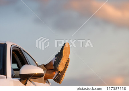 Man driver put feet on car window, relaxing, resting at sunset 137387338