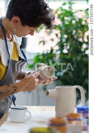 Ceramics hobby and small business: artisan woman model clay cap for pottery jug in artistic studio Ceramics hobby and small business: artisan woman model clay cap for pottery jug in artistic studio 137387346