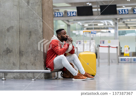 Tired Black tourist man on a long night connection at airport, waiting for plane sitting in terminal Tired Black tourist man on a long night connection at airport, waiting for plane sitting in terminal 137387367