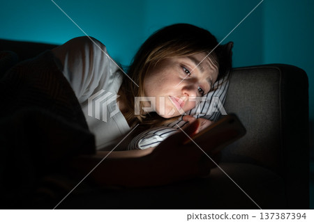 Woman using mobile phone while lying in bed at night, suffering from post-breakup insomnia. Anxiety. Woman using mobile phone while lying in bed at night, suffering from post-breakup insomnia. Anxiety. 137387394