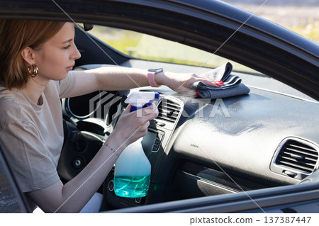 woman driver cleansing car dashboard with spray, wipes with microfiber from dust and dirt 137387447