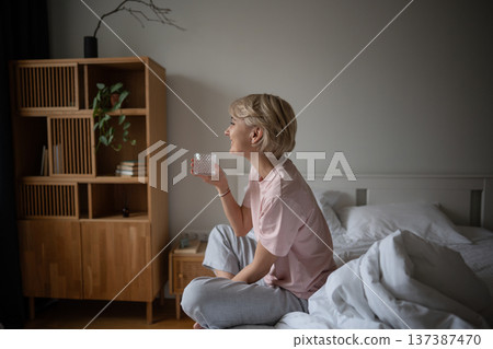 Smiling positive woman sitting in bed and drinking glass of water, enjoying relaxed morning time. Smiling positive woman sitting in bed and drinking glass of water, enjoying relaxed morning time. 137387470