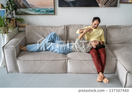 Happy married couple man and woman relaxing at home on sofa together, having fun smiling and joking. Happy married couple man and woman relaxing at home on sofa together, having fun smiling and joking. 137387480