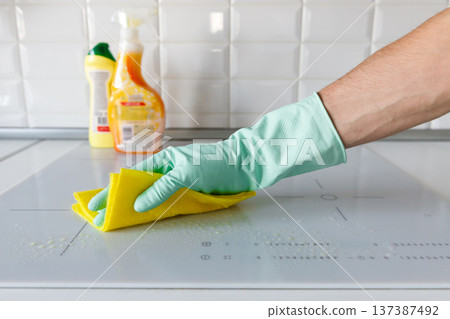 man hand in rubber gloves washing or cleaning induction hob 137387492