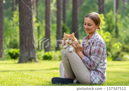 Smiling woman hugging and embracing domestic ginger cat, stroking on head, outdoors in sunny day Smiling woman hugging and embracing domestic ginger cat, stroking on head, outdoors in sunny day 137387512