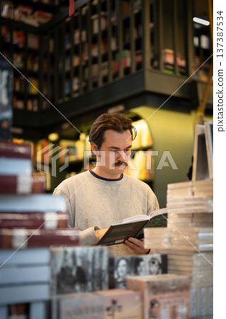 Man literature lover enjoying shopping in local bookstore, thinking and reading book from display. Man literature lover enjoying shopping in local bookstore, thinking and reading book from display. 137387534