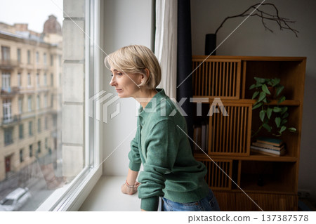 Smiling cheerful woman looking outside window enjoying morning city street view from apartment. 137387578