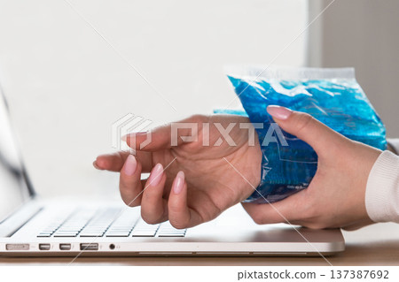 Woman applying cold compress to painful wrist caused by prolonged work on laptop. Arthritis Woman applying cold compress to painful wrist caused by prolonged work on laptop. Arthritis 137387692