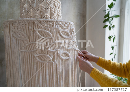 Clos up of woman working on half-finished macrame piece, weaves lamp shade for chandelier. hobby. Clos up of woman working on half-finished macrame piece, weaves lamp shade for chandelier. hobby. 137387717