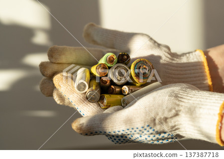 Close up of female hands in cotton protection gloves holding used alkaline batteries heap Close up of female hands in cotton protection gloves holding used alkaline batteries heap 137387718