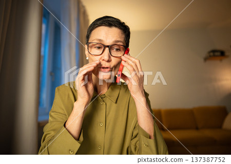 Feared senior woman talking on smartphone with financial scammers, giving away full bank information Feared senior woman talking on smartphone with financial scammers, giving away full bank information 137387752