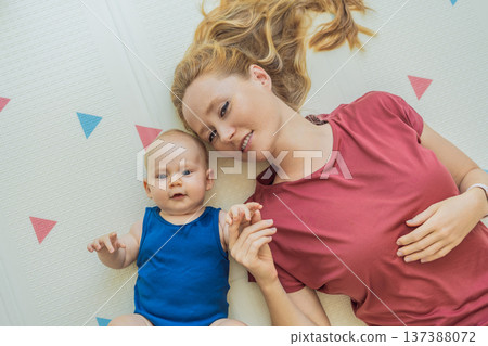 Mother and baby lying on a soft play mat at home, playing, talking and sharing a joyful moment together. Authentic family lifestyle, early childhood development and emotional bonding. Parenting and Mother and baby lying on a soft play mat at home, playing, talking and sharing a joyful moment together. Authentic family lifestyle, early childhood development and emotional bonding. Parenting and 137388072