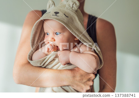 Mother holding her baby wrapped in a soft towel after bath at home, sharing a warm caring moment. Authentic parenthood scene showing love, safety and comfort. Baby hygiene, wellbeing and family 137388741