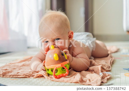 Little baby playing with toys on a soft baby play mat at home. Early childhood development, sensory play, learning through play, curiosity, and happy infant activity concept for modern parenting. 137388742