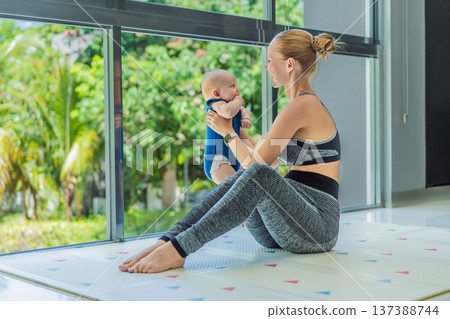 Mother doing fitness exercises while holding her baby at home, combining workout and childcare. Real lifestyle moment showing balance, strength and love. Postpartum fitness, healthy motherhood and Mother doing fitness exercises while holding her baby at home, combining workout and childcare. Real lifestyle moment showing balance, strength and love. Postpartum fitness, healthy motherhood and 137388744