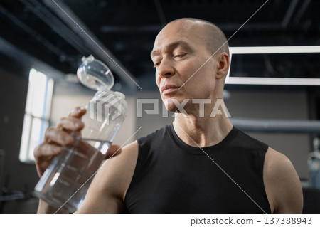 Athletic man checking shaker bottle after training in modern gym Athletic man checking shaker bottle after training in modern gym 137388943