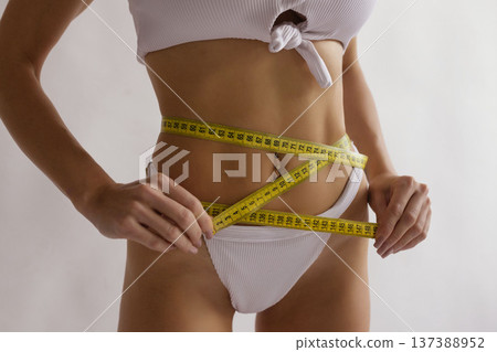 Slim female body with measuring tape around waist and hips, body care, weight loss and fitness diet concept Slim female body with measuring tape around waist and hips, body care, weight loss and fitness diet concept 137388952