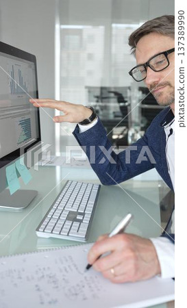 Businessman in a blue jacket analyzing financial data on computer, working in modern office, managing business strategy and reporting. Business people concept 137389990