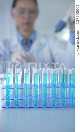 Test tubes with a blue liquid, close-up view. Scientist holding pipette conducting experiments in laboratory on the background. Science and Medicine 137390001