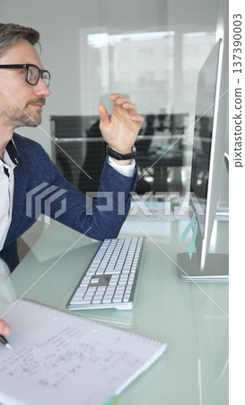 Professional man in a blue jacket working at office desk, analyzing documents and using computer for business productivity. Business people concept 137390003