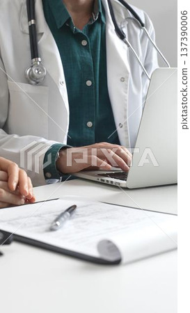 Doctor man wearing lab coat over a green shirt, is typing on a laptop and listening to a woman patient during medical consultation in clinic. Medicine and health care Doctor man wearing lab coat over a green shirt, is typing on a laptop and listening to a woman patient during medical consultation in clinic. Medicine and health care 137390006