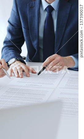 Businesspeople hands with pens reviewing documents and engaging in a discussion across a table, representing contract signing, legal consultation, negotiation, and important agreement collaboration 137390017