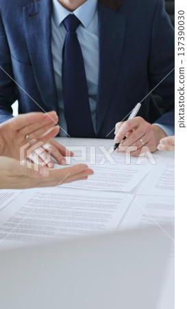 Businessman signing a contract papers at the white desk in office, colleagues applauding to the successful results of negotiations. Business people concept Businessman signing a contract papers at the white desk in office, colleagues applauding to the successful results of negotiations. Business people concept 137390030