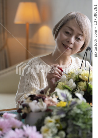 Senior woman making a flower arrangement as a hobby in the living room 137390261