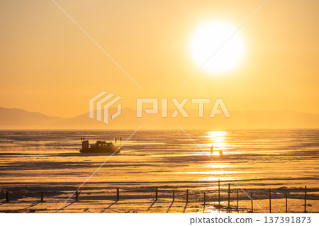 Scenery view of tourist walking on frozen lake Baikal during sunset seen from Listvyanka town, Russia. 137391873