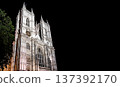 Historic gothic cathedral architecture illuminated at night under a dramatic sky, highlighting intricate stone design and timeless European heritage. 137392170