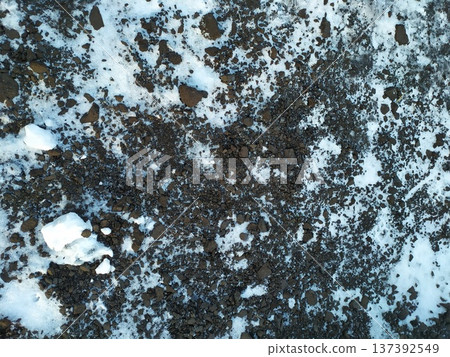 Texture of snowy ground with dark dirt and rocks. Winter background pattern 137392549