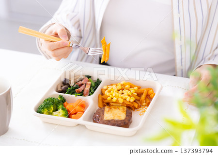 一位女士正在吃外帶午餐,她的手放在她的手上 一位女士正在吃外帶午餐,她的手放在她的手上 137393794