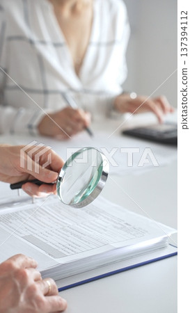 Team of accountants are working together, using a magnifying glass and a calculator, to audit financial reports in office. Audit and taxes concept 137394112