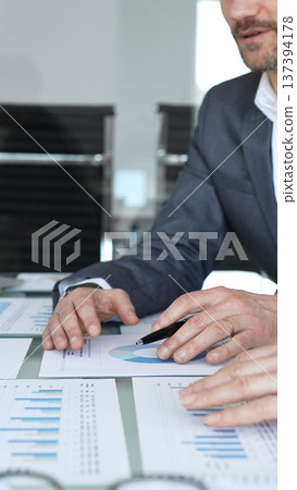 Businessman's hands analyzing financial data and charts on documents during a meeting, focusing on strategic planning and corporate growth in an office setting Businessman's hands analyzing financial data and charts on documents during a meeting, focusing on strategic planning and corporate growth in an office setting 137394178