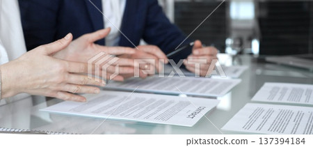 Close-up view of a business person in a professional office setting, reviewing and signing a legal contract document. Hands holding a pen over paperwork during corporate deal negotiations 137394184