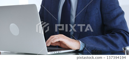 Professional businessman working on laptop computer, typing on keyboard at modern office desk, managing business tasks. Business people concept Professional businessman working on laptop computer, typing on keyboard at modern office desk, managing business tasks. Business people concept 137394194