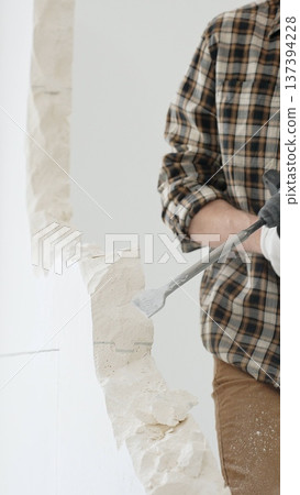 Close up of unrecognizable male construction worker wearing beige checkered shirt and protective gloves, is demolishing white wall with rotary hammer drill, generating dust. Renovation concept 137394228