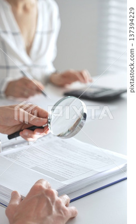 Team of accountants are working together, using a magnifying glass and a calculator, to audit financial reports in office. Audit and taxes concept Team of accountants are working together, using a magnifying glass and a calculator, to audit financial reports in office. Audit and taxes concept 137394229