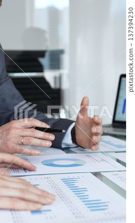 Business professionals analyzing financial data on a digital tablet and printed charts, collaborating on strategy and planning during a corporate meeting in an office setting Business professionals analyzing financial data on a digital tablet and printed charts, collaborating on strategy and planning during a corporate meeting in an office setting 137394230