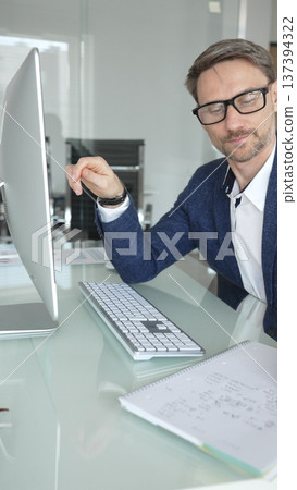 Businessman in a blue jacket analyzing financial data on computer, working in modern office, managing business strategy and reporting. Business people concept Businessman in a blue jacket analyzing financial data on computer, working in modern office, managing business strategy and reporting. Business people concept 137394322