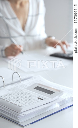 Close up of a calculator on financial documents, with an accountant taking notes, emphasizing accounting, finance, and tax preparation. Audit and taxes in business Close up of a calculator on financial documents, with an accountant taking notes, emphasizing accounting, finance, and tax preparation. Audit and taxes in business 137394345