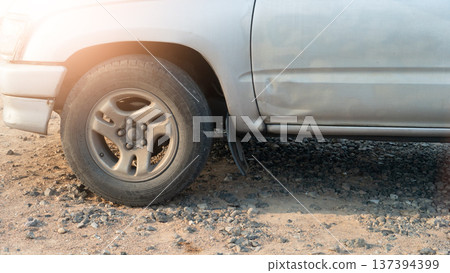 Close up on wheels of an old car. A side view of a pickup truck. A vehicle parked on the ground covered in rocks. Close up on wheels of an old car. A side view of a pickup truck. A vehicle parked on the ground covered in rocks. 137394399