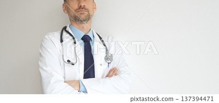 Headshot of a confident doctor man wearing stethoscope and white coat, is standing with crossed arms, representing medical professionalism and expertise. Medicine and health care Headshot of a confident doctor man wearing stethoscope and white coat, is standing with crossed arms, representing medical professionalism and expertise. Medicine and health care 137394471