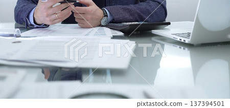 Businessman wearing blue suit is working with laptop, calculator and documents in a professional office setting. Low lighting, close-up view. Business people, audit concept 137394501