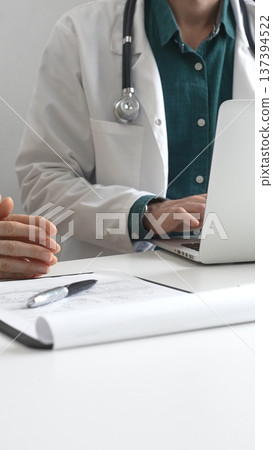 Doctor man wearing lab coat over a green shirt, is typing on a laptop and listening to a woman patient explaining symptoms during medical consultation in clinic. Medicine and health care concept 137394522