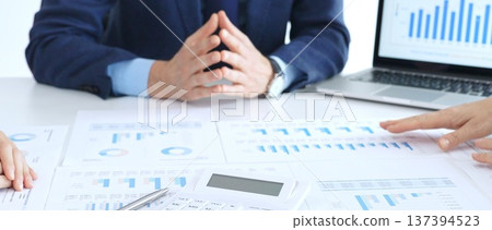 Business people reviewing financial charts and reports in office, using a laptop and calculator while engaging in discussions about strategy and performance Business people reviewing financial charts and reports in office, using a laptop and calculator while engaging in discussions about strategy and performance 137394523